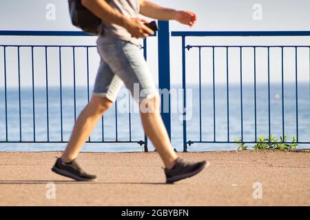 Mann mit Jeans-Shorts und Rucksack an einem sonnigen Morgen am Meer im Sommer zu Fuß Stockfoto