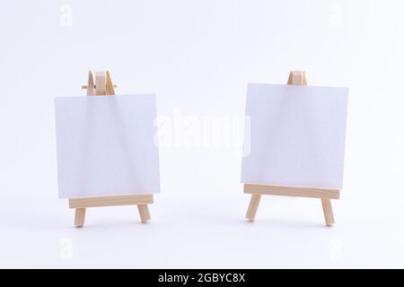 Zwei hölzerne Easels Miniature mit blanker weißer quadratischer Leinwand für Künstler und Maler - Mockup. Mini-Holzständer mit sauberer Zeichenfläche auf weißem Hintergrund, Copy Space Stockfoto