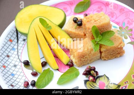 Nahaufnahme der in Scheiben geschnittenen grünen gelben Mango mit Milchkuchen süßen grünen j amble Frucht und Minzblätter über unscharf weiß braunen Hintergrund. Stockfoto