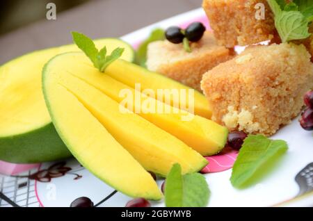 Nahaufnahme der in Scheiben geschnittenen grünen gelben Mango mit Milchkuchen süßen grünen j amble Frucht und Minzblätter über unscharf weiß braunen Hintergrund. Stockfoto