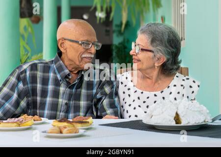 Ein älteres Paar mit Brille sitzt an einem Tisch, beide lächeln Stockfoto