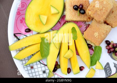 Nahaufnahme der in Scheiben geschnittenen grünen gelben Mango mit Milchkuchen süßen grünen j amble Frucht und Minzblätter über unscharf weiß braunen Hintergrund. Stockfoto