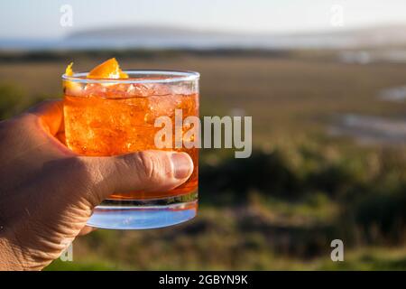 Eine Hand mit einem Whisky-Cocktail aus Orange, serviert in einer Außenbar in Bodega Bay, Kalifornien Stockfoto