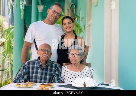 Ein älteres Paar mit Brille sitzt an einem Tisch und ein Mann und eine junge Frau stehen hinter den älteren Menschen Stockfoto