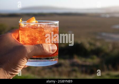 Eine Hand mit einem Whisky-Cocktail aus Orange, serviert in einer Außenbar in Bodega Bay, Kalifornien Stockfoto