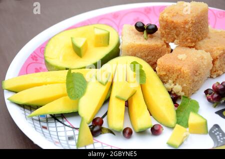 Nahaufnahme der in Scheiben geschnittenen grünen gelben Mango mit Milchkuchen süßen grünen j amble Frucht und Minzblätter über unscharf weiß braunen Hintergrund. Stockfoto