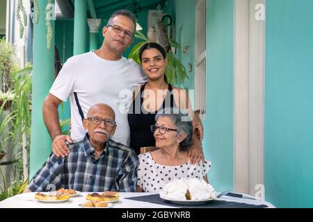 Ein älteres Paar mit Brille sitzt an einem Tisch und ein Mann und eine junge Frau stehen hinter den älteren Menschen Stockfoto