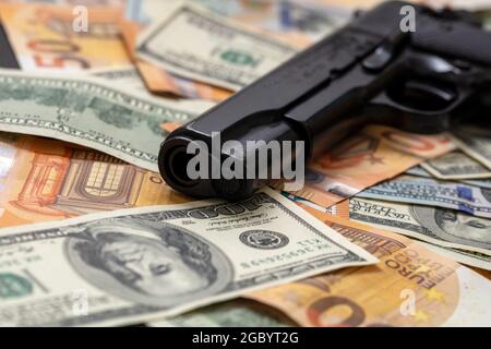 Pistole auf Dollar- und Euro-Banknoten im Hintergrund, Nahaufnahme. Kriminelles Geld. Schwarzgeld und Schutz, Mafia- und Korruptionskonzept, Stockfoto