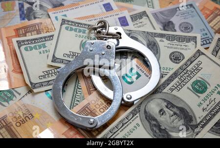 Geld und Verbrechen. Handschellen auf US-Dollar- und Euro-Banknoten im Hintergrund. Bestechung, Korruption und Gerechtigkeit. Stockfoto