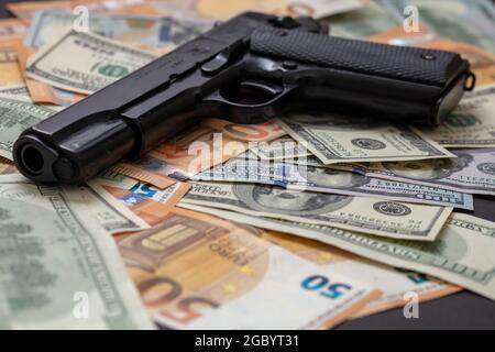 Pistole auf Dollar- und Euro-Banknoten im Hintergrund, Nahaufnahme. Kriminelles Geld. Schwarzgeld und Schutz, Mafia- und Korruptionskonzept, Stockfoto