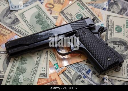 Schwarzgeld und Schutz, Mafia- und Korruptionskonzept, Pistole auf Dollar- und Euro-Banknoten Hintergrund, Nahaufnahme. Kriminelles Geld. Stockfoto