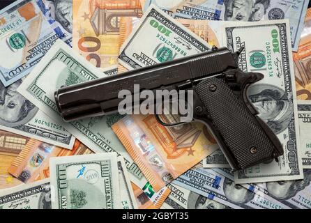 Kriminelles Geld. Pistole auf Dollar- und Euro-Banknoten im Hintergrund, Draufsicht. Mafia- und Korruptionskonzept, Schwarzgeld und Schutz Stockfoto