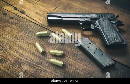 Pistolenpistole 9mm und Munitionsgeschosse auf Holzhintergrund. Schwarze Metallwaffe, automatische Handfeuerwaffe für Militär und Sicherheit auf einem Vintage-Tisch. Seitenansicht Stockfoto