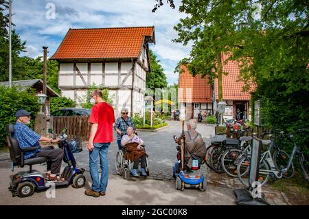 BIELEFELD, DEUTSCHLAND. 20. JUNI 2021 Loheide Park. Rentner fahren einen Elektroroller, eine Frau trägt eine alte Dame im Rollstuhl, Männer reden. Stockfoto