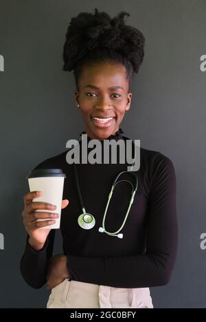 Lächelnde afrikanische Ärztin mit Stethoskop und einer Tasse Kaffee. Stockfoto