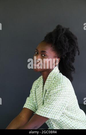Porträt einer jungen afrikanischen Frau, die lächelnd auf einem Stuhl sitzt und eine grüne Jacke trägt. Stockfoto