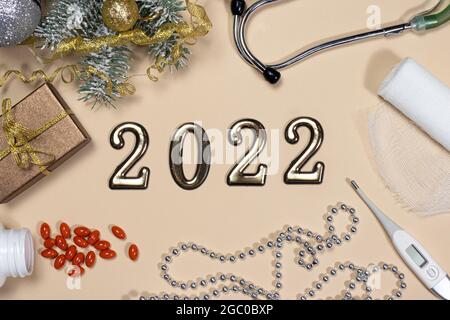 Medizin für das neue Jahr 2022. Karte zu medizinischen Themen: Phonendoskop, Tabletten, Thermometer und Verband mit Fichtenzweig auf beigem Hintergrund. Stockfoto