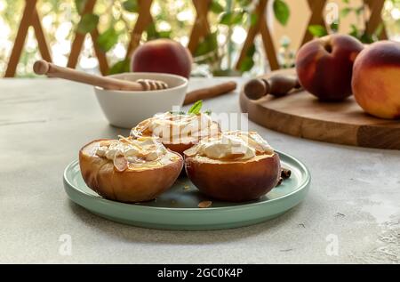 Gebackene reife Pfirsiche mit Zimt, Mandelblüten, Frischkäse und Honig in einem Sommergarten. Selektiver Fokus Stockfoto