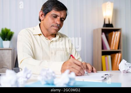 Geschäftsmann, der für eine neue Idee oder ein Projekt plant, arbeitet hart, indem er denkt, auf Papier schreibt und Papier um den Tisch schmettert - Konzept, um Probleme zu lösen Stockfoto