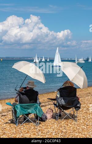 cowes Week, Insel der wight, Segelregatta, Segelregatta, älteres Paar zuschauend, Pärchen sitzt unter Sonnenschirmen, Pärchen sitzt im Schatten. Stockfoto