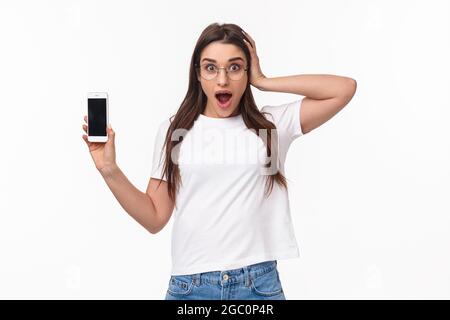 Kommunikations-, Technologie- und Lifestyle-Konzept. Waist-up-Porträt von erstaunt überrascht und aufgeregt junge Frau in einer Brille, keuchen und berühren Kopf Stockfoto