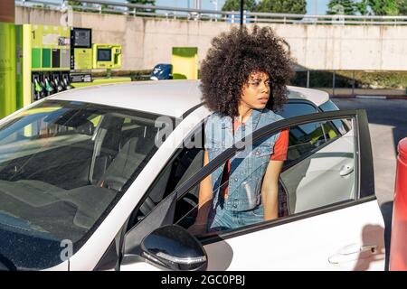 Junge afrikanerin mit afro Haaren kam in ihr Auto, nachdem sie ihr Auto in der Tankstelle mit Gas gefüllt hatte. Stockfoto