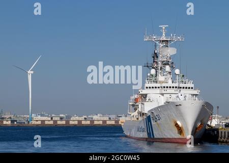 Ein Schiff der japanischen Küstenwache, Shikishima (PLH 31) vor einer Windturbine in Yokohama Bay, Yokohama, Kanagawa, Japan. Stockfoto