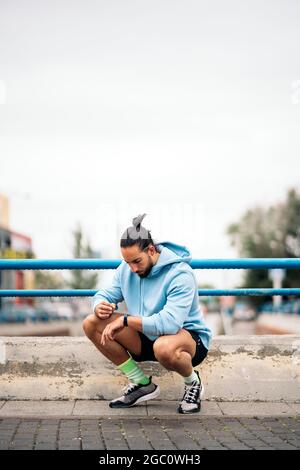 Schöner Mann mit Sportkleidung, der seine Smart-Watch verwendet und sich nach dem Laufen in der Stadt ausruhte. Stockfoto