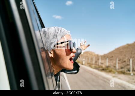 asiatische Frau Touristen, die den Kopf aus der Heckscheibe eines Autos ragt und eine Autoreise genießt Stockfoto