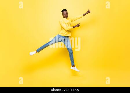 Junger energischer afrikanischer Mann springt und zeigt die Hände auf isolierten gelben Studiohintergrund Stockfoto
