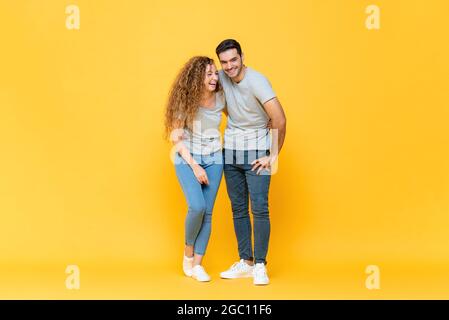 In voller Länge Porträt von jungen glücklich interracial Millennial Paar halten sich gegenseitig und lachen in isolierten gelben Studio Hintergrund Stockfoto