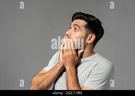 Schockiert verängstigten jungen kaukasischen Mann mit Augen knallen und Hände decken den Mund auf hellgrauen Studio Hintergrund Stockfoto