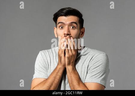 Schockiert verängstigten jungen kaukasischen Mann mit Augen knallen und Hände decken den Mund auf hellgrauen Studio Hintergrund Stockfoto