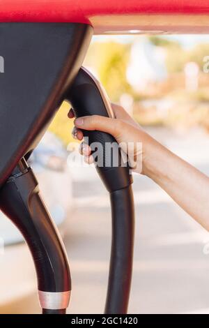 Frauenhand, die eine EV- oder Elektroautosteckdose in einer Ladestation hält. Stromversorgung in einem Kraftwerk und umweltfreundliche Alternative energ Stockfoto