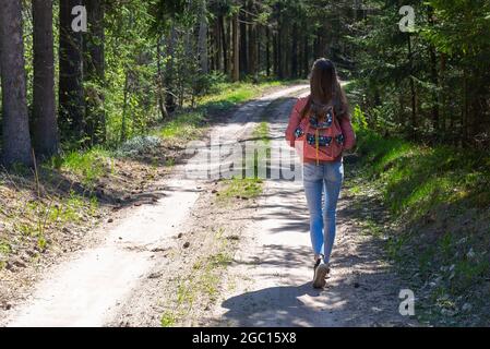 Ein junges Mädchen mit Rucksack zu Fuß entlang Weg durch den Wald während des Sommers. Hipster Lifestyle und Solo Trip.Rückansicht. Stockfoto