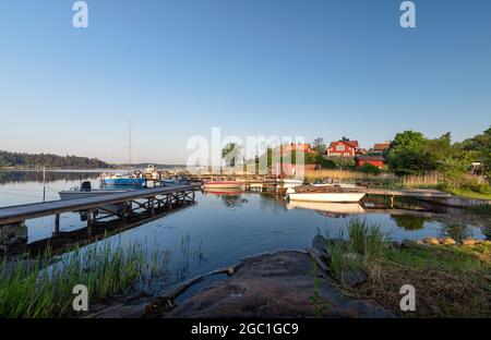 Sommer in schwedischer Landschaft - Morgenlandschaft mit Booten und traditionellen roten Häusern. Urlaub auf dem Stockholmer Archipel in der Ostsee, gemütliches Scandin Stockfoto