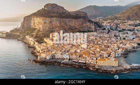 Sonnenaufgang über dem Hafen in Cefalu, Sizilien, Italien, Panorama-Luftaufnahme der Altstadt mit bunten Häusern am Wasser, Meer und La Rocca Klippe.attraktiv Stockfoto