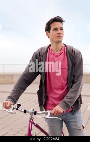 Vertikales Porträt eines hübschen jungen Mannes, der mit einem Vintage-Fahrrad läuft, Konzept für nachhaltigen Transport und urbanen Lebensstil Stockfoto