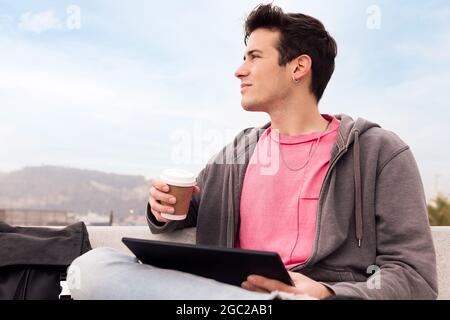 Junger Mann, der mit einem Tablet im Freien sitzt, mit Kaffee, Konzept von Technologie und urbanem Lebensstil, Platz für Text kopieren, Platz für Text kopieren Stockfoto
