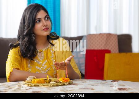 EINE JUNGE FRAU, DIE NACH OBEN SCHAUT UND RAKHI IN DER HAND HÄLT Stockfoto