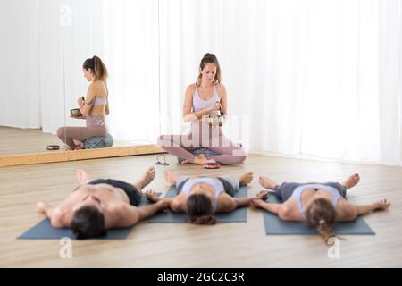 Yogalehrer und Gruppe junger sportlicher Menschen im Yoga-Studio, liegen und entspannen auf Yogamatten während der erholsamen Yoga-Sitzung. Gesund aktiv Stockfoto