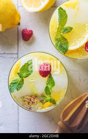 Hausgemachte Limonade mit Minze und Himbeeren in Gläsern, graue Fliesen Hintergrund, Draufsicht. Konzept für kalte Sommergetränke. Stockfoto