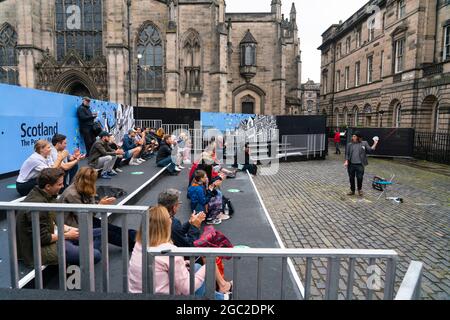 Edinburgh, Schottland, Großbritannien. August 2021. Bilder von der Royal Mile in der Altstadt von Edinburgh am Eröffnungstag des Edinburgh Fringe Festivals 2021. Das Festival sieht ganz anders aus als vor zwei Jahren. Nur sehr wenige Straßenaufführungsräume sind erlaubt und deutlich weniger Touristen sind zu sehen. Auch eine hohe Sichtbarkeit der Polizei, es gibt mehr Polizeibeamte als Darsteller auf der Straße, steht in einem deutlichen Kontrast zu den Vorjahren. PIC; Performer unterhält die Menge in speziell dafür eingerichteten, abgeschirmten Veranstaltungsräumen im Freien, die die Kapazität des Publikums einschränken. Iain Masterton/Alamy Live Nachrichten. Stockfoto