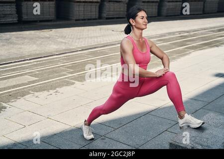 Gesammelter Fitnesspraktiker, der auf der Straße Bein streckt Stockfoto