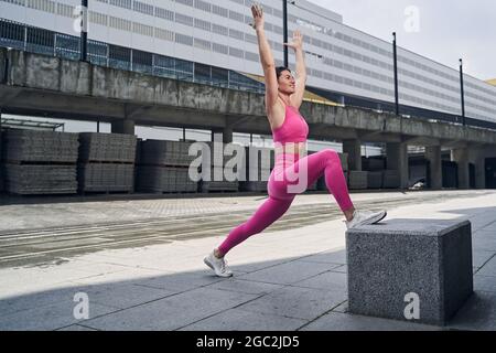 Sportler legt das rechte Bein auf Stein und hebt die Arme Stockfoto