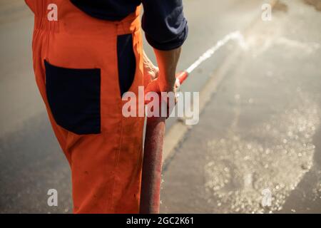 Wasserschlauch. Der Wasserfluss aus dem Rohr. Ein Mann hält einen Feuerwehrschlauch. Stockfoto