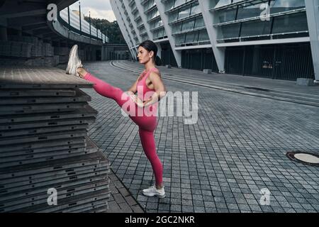 Frau, die ihr Bein während des Dehnens auf Betonblöcken zerren wird Stockfoto