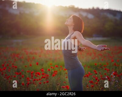 Junge schöne Frau mit erhobenen Armen im Frühjahr Mohnfeld. Sanfte Farben. Nachdenkliche, entspannte Atmosphäre. Stockfoto