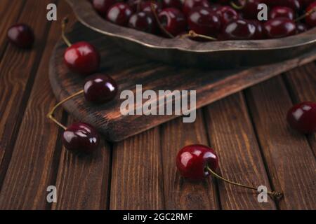 Frische Bio-rote Kirschfrüchte in einem Vintage-Silberteller auf einem alten, strukturierten Holzschneidebrett auf einem Tisch aus Holzbrettern Stockfoto