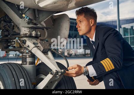 Seriöser lizenzierter Flieger, der das Fahrwerk inspiziert Stockfoto